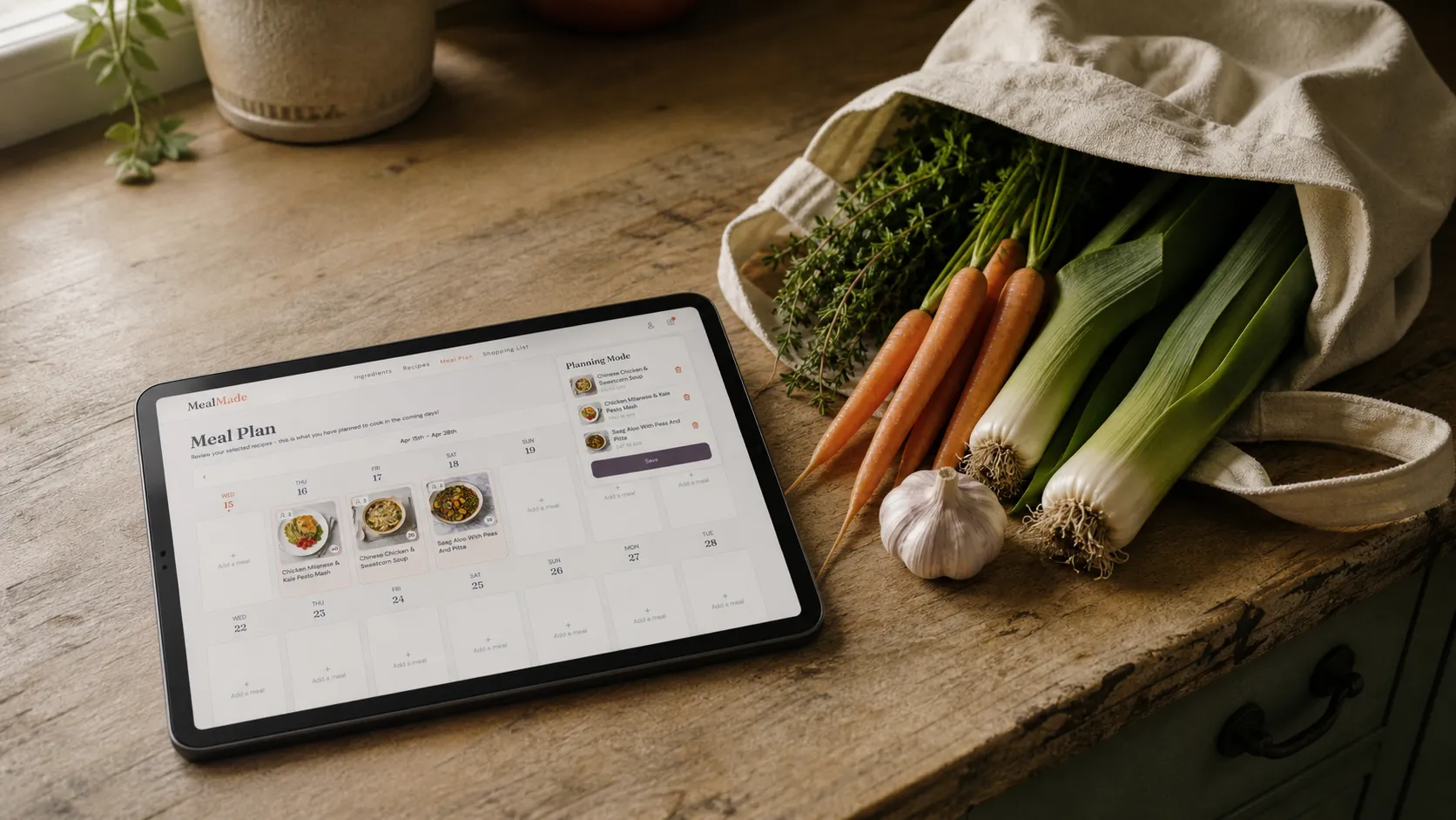 A meal plan and shopping list open on a tablet next to a canvas tote bag and fresh vegetables on a kitchen counter